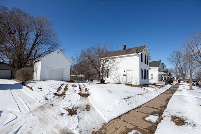 view of snowy exterior featuring an outbuilding, a detached garage, and a chimney