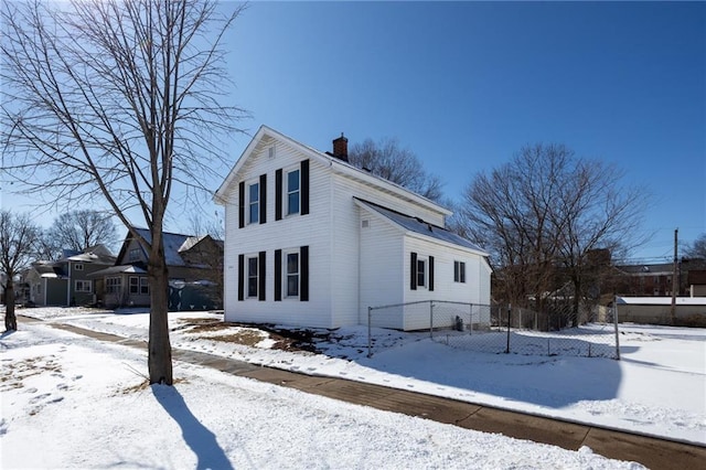 view of snowy exterior with a chimney and fence