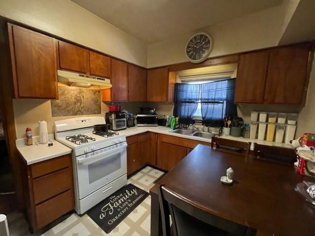 kitchen with under cabinet range hood, white range with gas stovetop, a sink, brown cabinets, and light floors