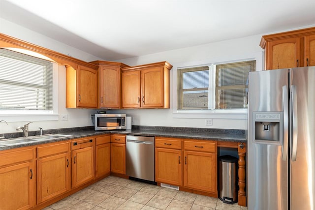 kitchen with dark countertops, brown cabinetry, stainless steel appliances, and a sink