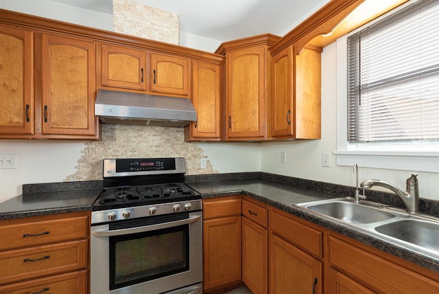 kitchen with under cabinet range hood, stainless steel gas range, brown cabinets, and a sink