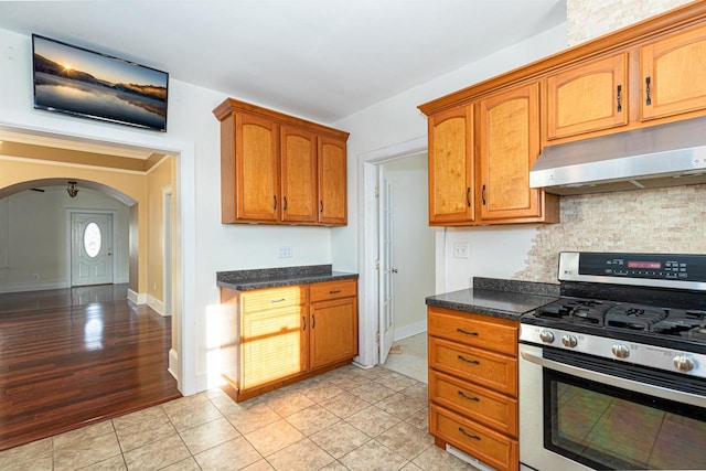 kitchen with arched walkways, light tile patterned floors, backsplash, stainless steel range with gas stovetop, and under cabinet range hood