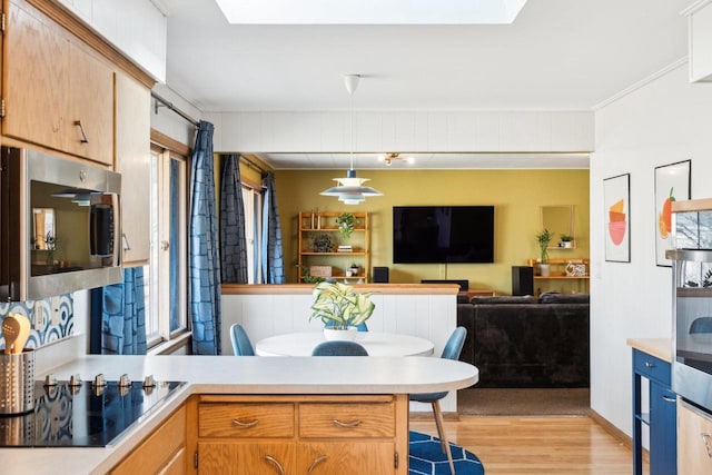 kitchen featuring light wood finished floors, stainless steel microwave, light countertops, a peninsula, and black electric cooktop