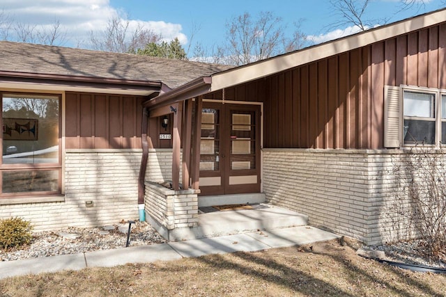 view of exterior entry with board and batten siding, brick siding, and roof with shingles