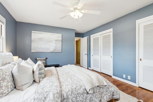 bedroom featuring baseboards, a ceiling fan, multiple closets, and wood finished floors