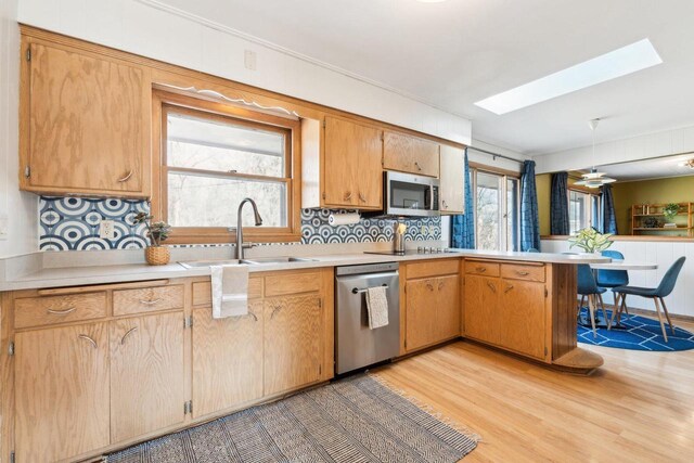 kitchen with light countertops, a peninsula, a skylight, stainless steel appliances, and a sink