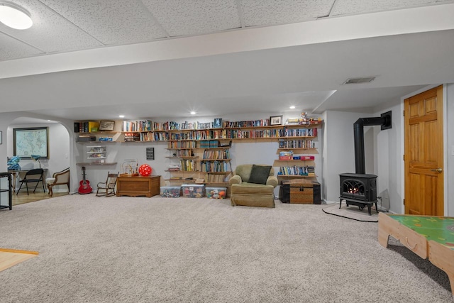 below grade area featuring visible vents, carpet floors, arched walkways, a paneled ceiling, and a wood stove