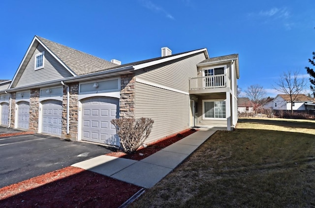 exterior space with aphalt driveway, a lawn, a balcony, a garage, and stone siding