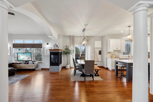 dining space featuring dark wood-type flooring, decorative columns, and a multi sided fireplace