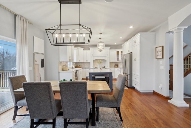 dining room with decorative columns, baseboards, wood finished floors, and stairs