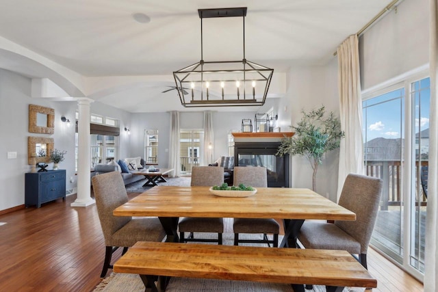 dining room featuring light wood finished floors, baseboards, a multi sided fireplace, decorative columns, and arched walkways