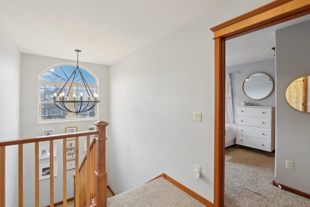 corridor featuring an upstairs landing, baseboards, an inviting chandelier, and carpet floors