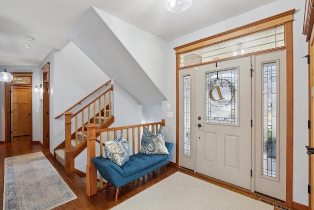 foyer entrance with visible vents, baseboards, wood finished floors, and stairs