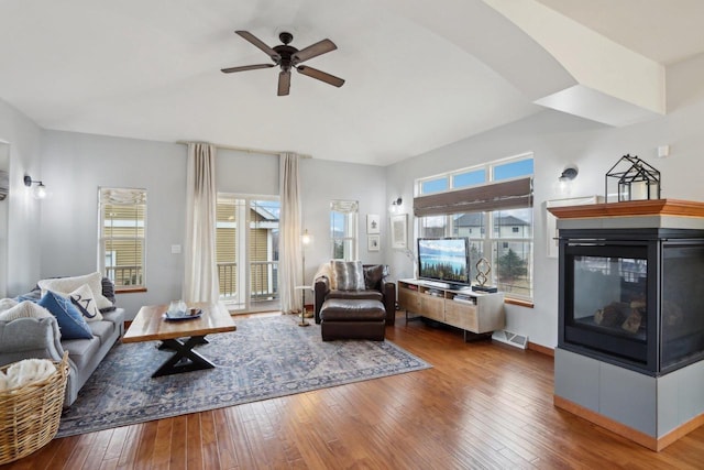 living room with visible vents, baseboards, ceiling fan, a multi sided fireplace, and wood-type flooring