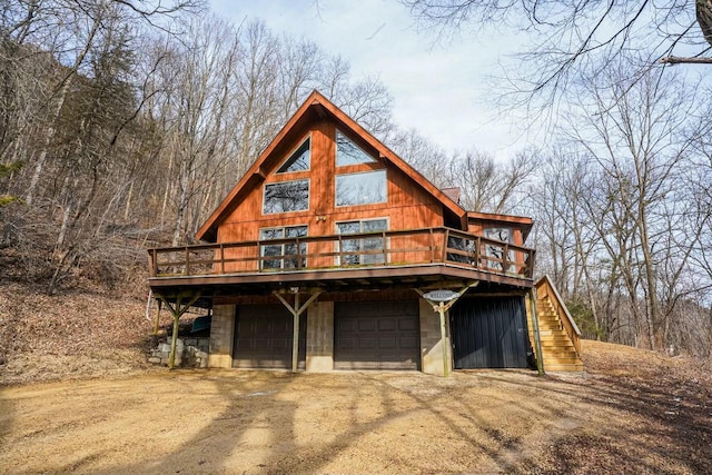 view of front facade featuring a garage, a wooden deck, dirt driveway, and stairs