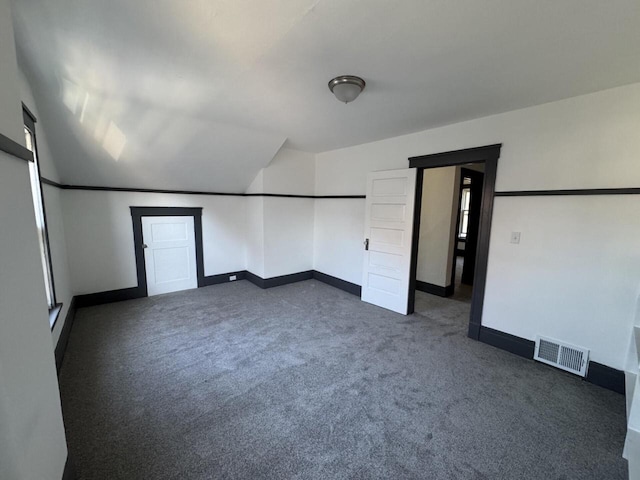 interior space with baseboards, vaulted ceiling, visible vents, and dark carpet