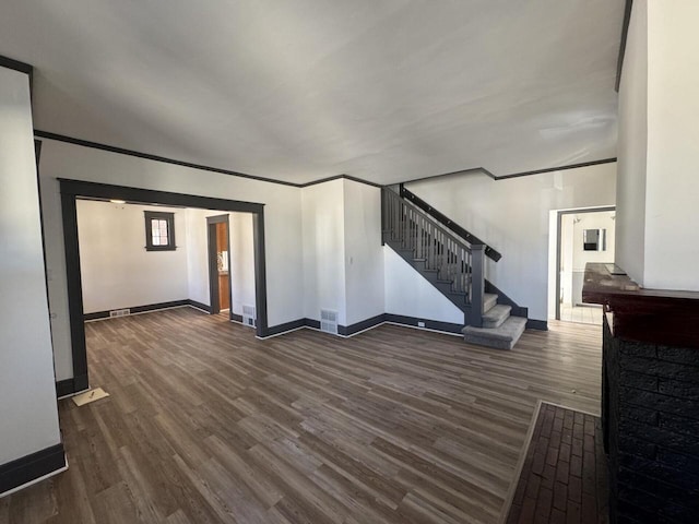 unfurnished living room with dark wood-style floors, crown molding, stairway, and baseboards