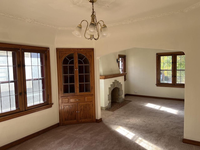 unfurnished living room with baseboards, carpet floors, a fireplace with flush hearth, and a notable chandelier