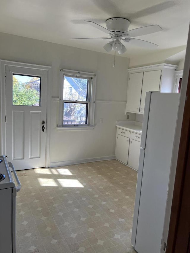 kitchen featuring baseboards, white cabinets, range, freestanding refrigerator, and light countertops