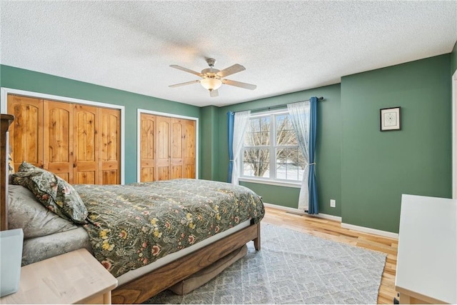 bedroom featuring multiple closets, ceiling fan, a textured ceiling, wood finished floors, and baseboards