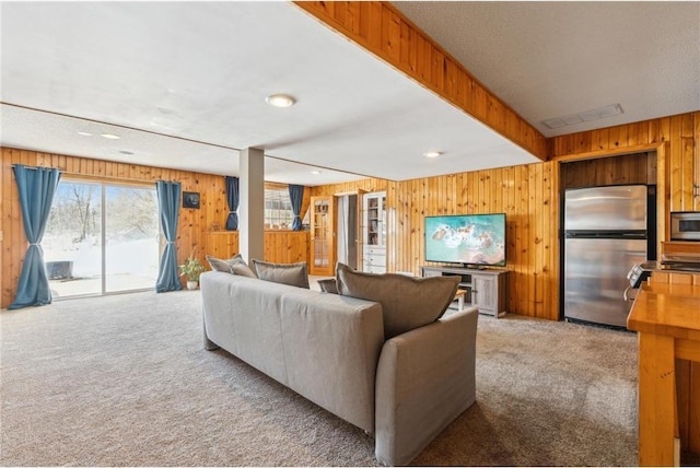 carpeted living area with recessed lighting, beam ceiling, visible vents, and wood walls