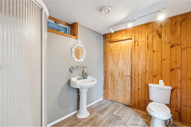 full bathroom featuring wooden walls, baseboards, toilet, wood finished floors, and a textured ceiling