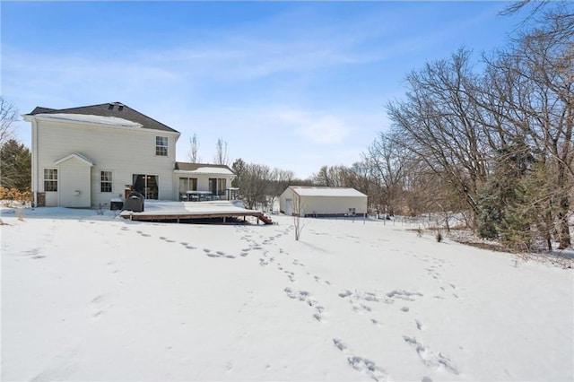 snow covered rear of property with a storage shed, a wooden deck, and an outdoor structure