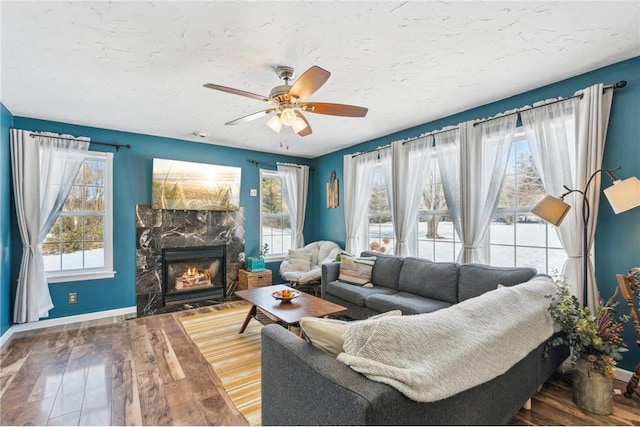 living area featuring a fireplace with flush hearth, a ceiling fan, a textured ceiling, wood finished floors, and baseboards