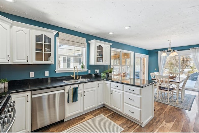 kitchen with stainless steel appliances, a peninsula, a sink, dark countertops, and glass insert cabinets