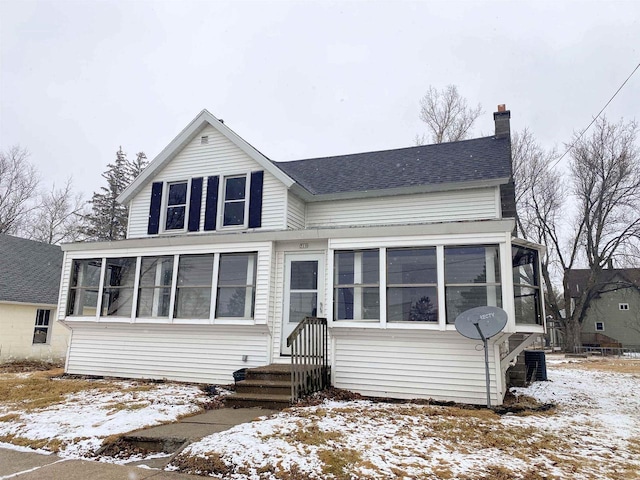 view of front of home featuring a shingled roof, cooling unit, a sunroom, and a chimney