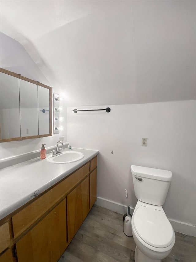 bathroom featuring lofted ceiling, toilet, wood finished floors, vanity, and baseboards