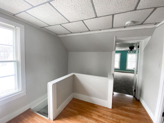 hallway featuring a drop ceiling, wood finished floors, an upstairs landing, and baseboards