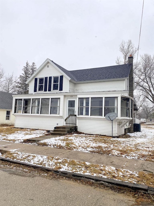 view of front of property featuring a sunroom, a chimney, and central air condition unit