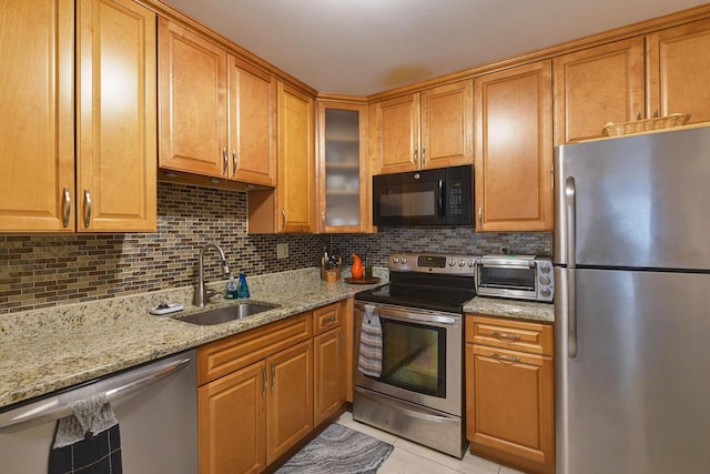 kitchen featuring a toaster, decorative backsplash, appliances with stainless steel finishes, light stone countertops, and a sink