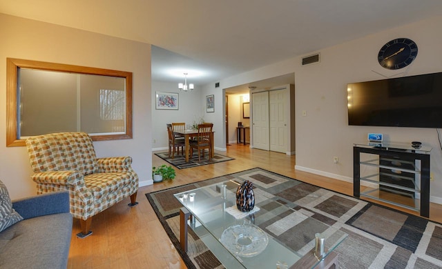 living area featuring an inviting chandelier, baseboards, visible vents, and wood finished floors