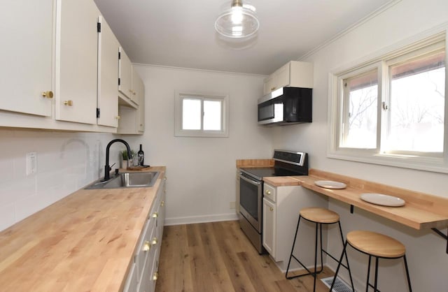 kitchen with a sink, appliances with stainless steel finishes, wood counters, white cabinetry, and tasteful backsplash