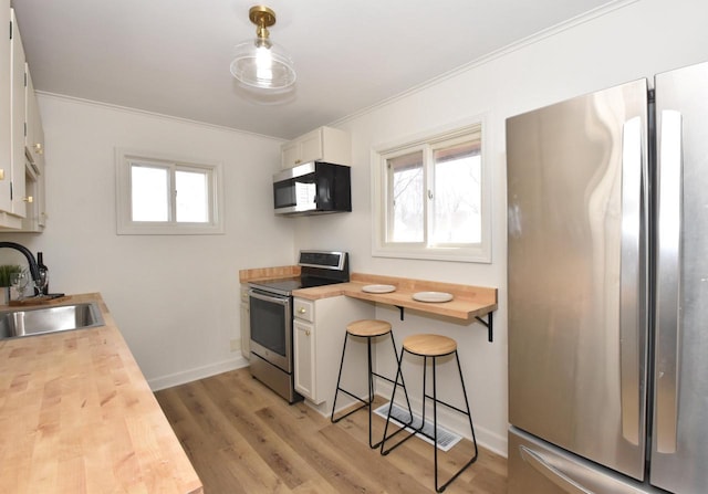 kitchen with wooden counters, a sink, stainless steel appliances, crown molding, and light wood-type flooring