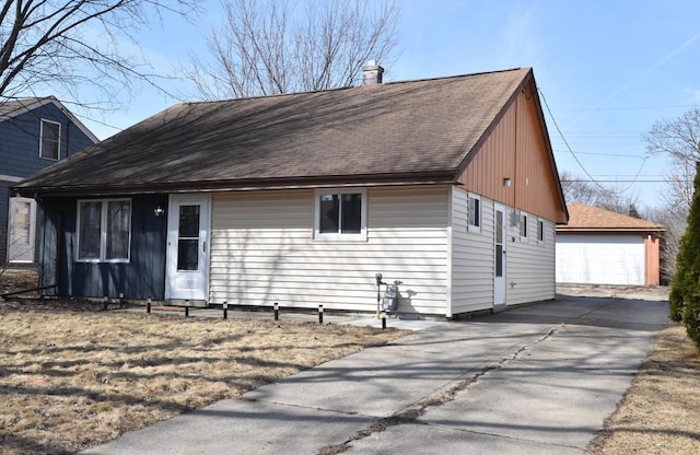 view of front of home featuring an outbuilding, a chimney, a garage, and a shingled roof