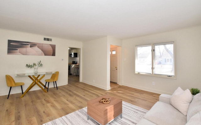 living room with visible vents, light wood-style floors, and baseboards