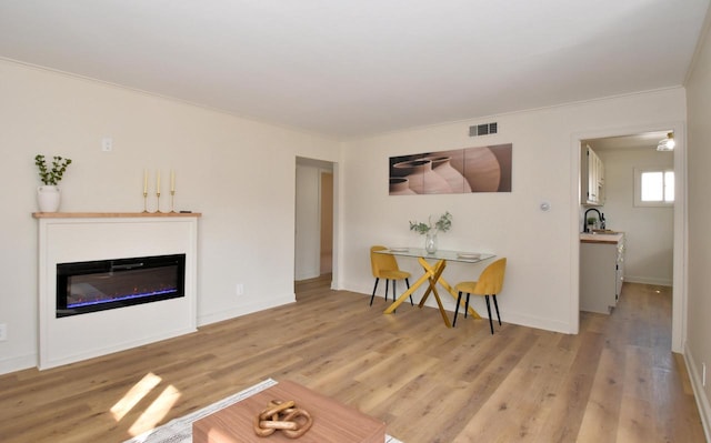 living area featuring a glass covered fireplace, visible vents, light wood-type flooring, and baseboards