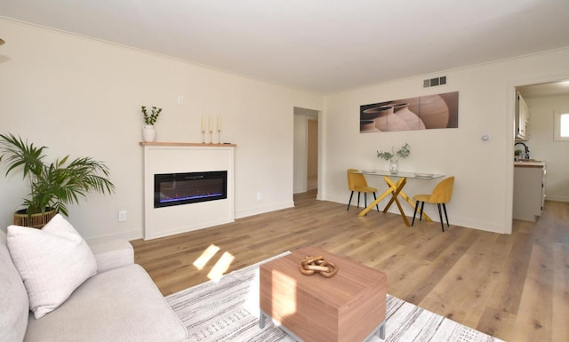 living area featuring a glass covered fireplace, light wood-style flooring, visible vents, and baseboards