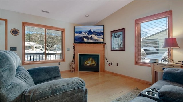 living area with lofted ceiling, wood finished floors, visible vents, baseboards, and a glass covered fireplace