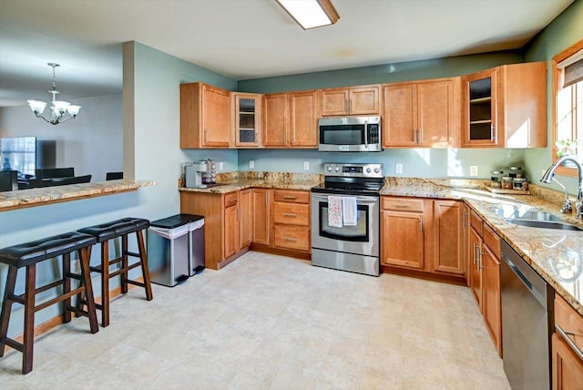 kitchen featuring a sink, glass insert cabinets, light stone countertops, and appliances with stainless steel finishes