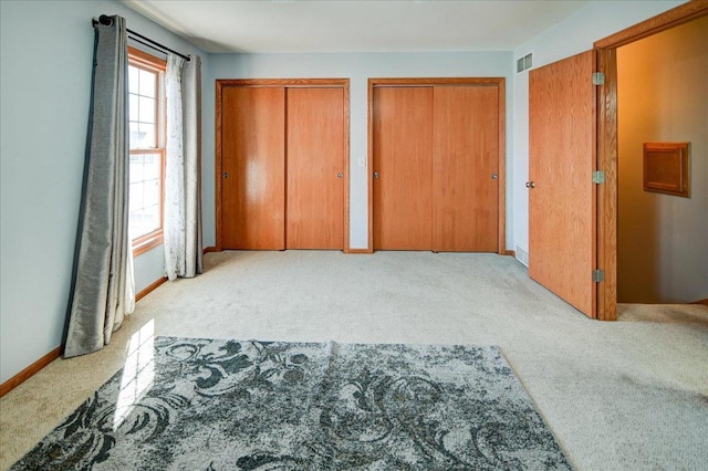 carpeted bedroom with visible vents, two closets, and baseboards