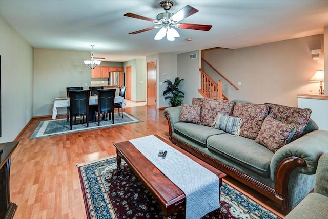 living area featuring visible vents, light wood-style flooring, ceiling fan with notable chandelier, stairway, and baseboards