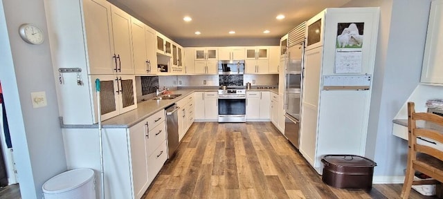 kitchen with recessed lighting, appliances with stainless steel finishes, glass insert cabinets, a sink, and wood finished floors