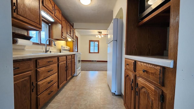 kitchen with white appliances, baseboards, arched walkways, a sink, and light countertops