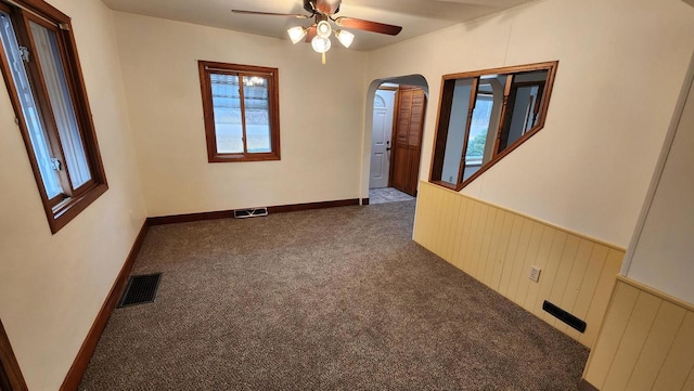 empty room featuring visible vents, arched walkways, carpet, and a wainscoted wall