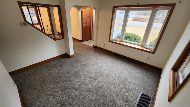 carpeted spare room with visible vents, arched walkways, and baseboards