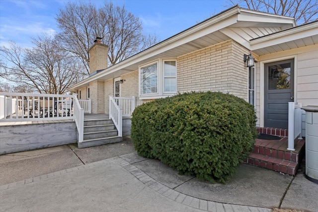 view of exterior entry with a wooden deck, brick siding, and a chimney